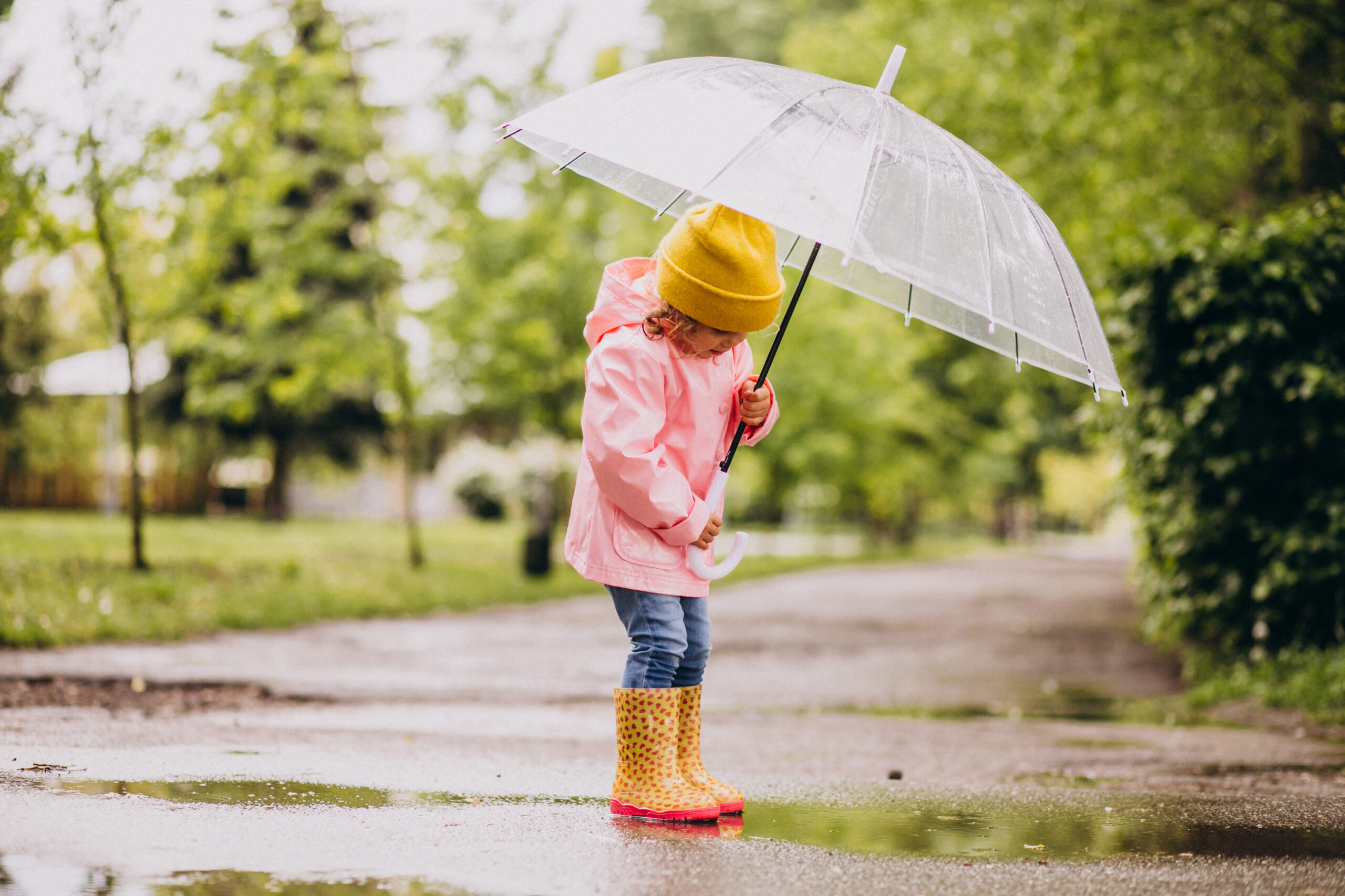 Cute little girl jumping into puddle in a rainy weather